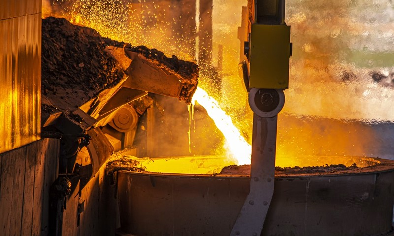 Molten metal pouring from a furnace into a large industrial ladle