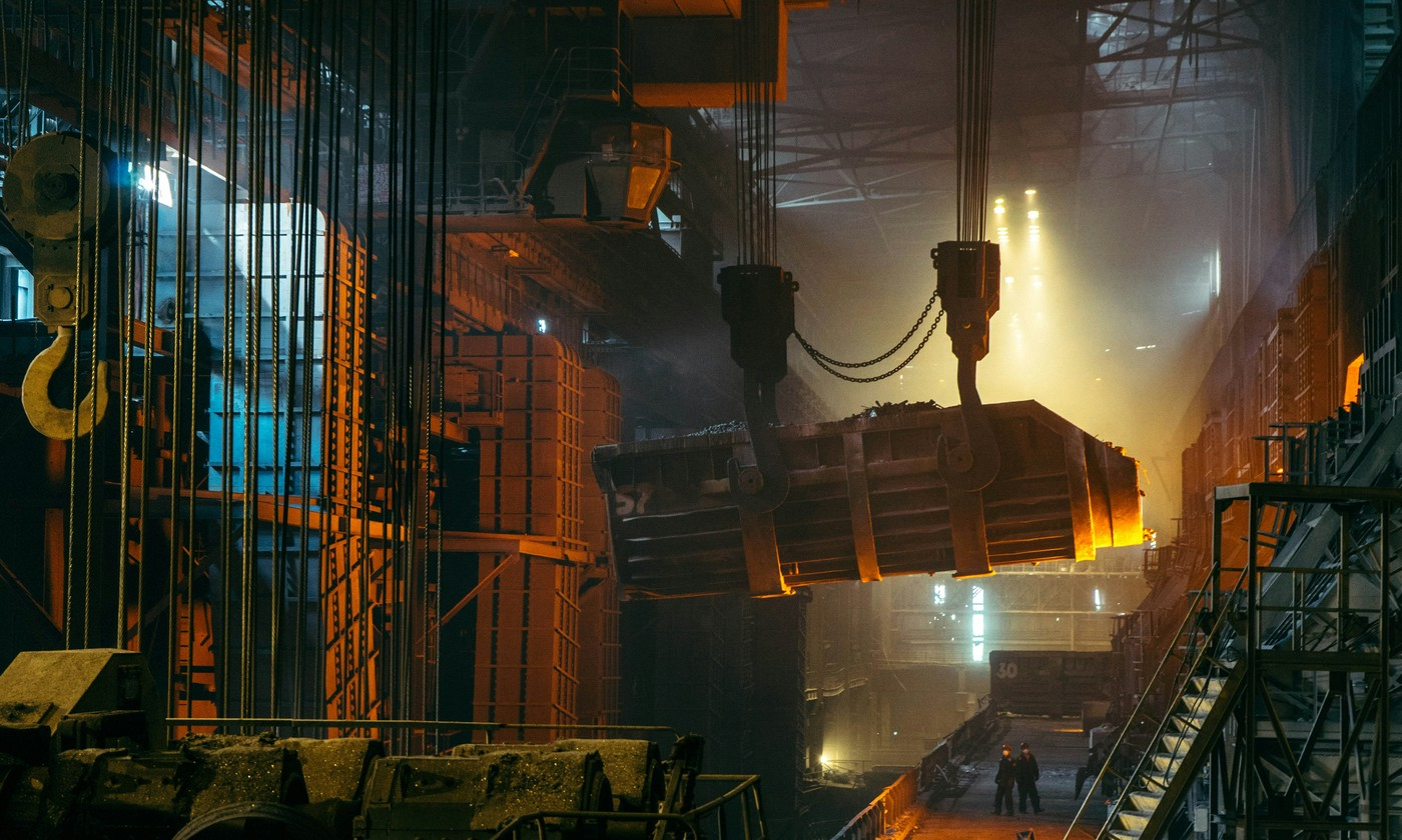 Heavy industrial crane lifting a glowing molten metal ladle in a steel mill